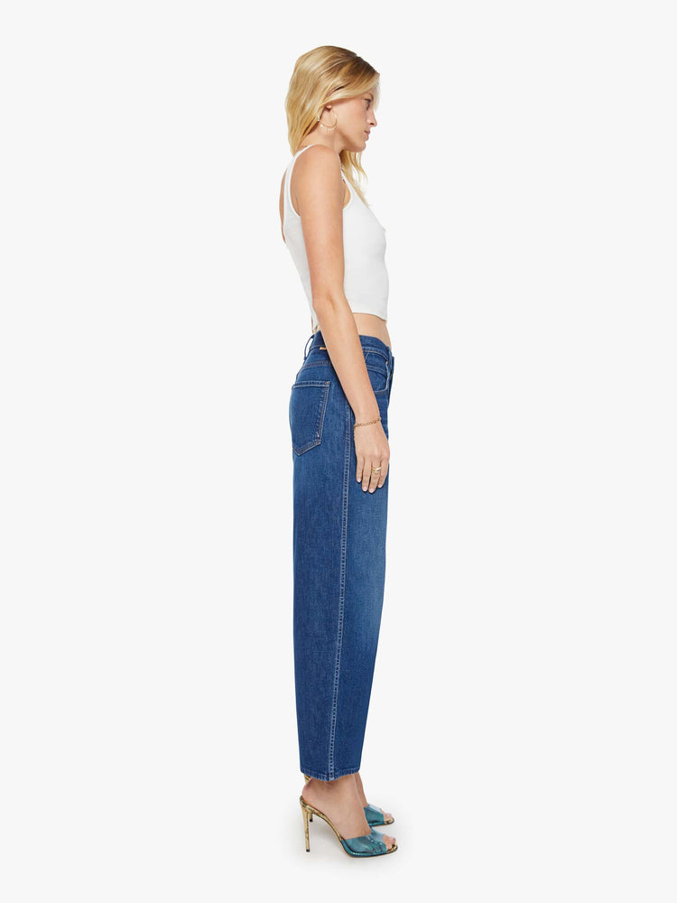 Side view of a woman in a dark blue jeans designed to sit lower on the hips with an ankle-length inseam, zip fly, clean hem and slightly tapered leg.