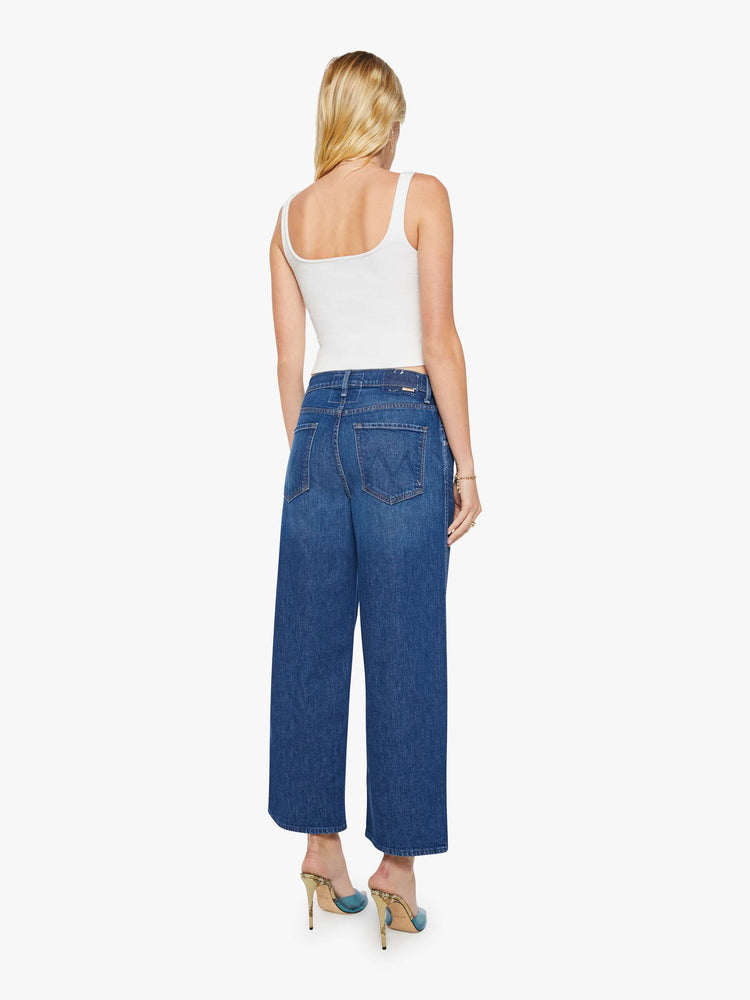 Back view of a woman in a dark blue jeans designed to sit lower on the hips with an ankle-length inseam, zip fly, clean hem and slightly tapered leg.