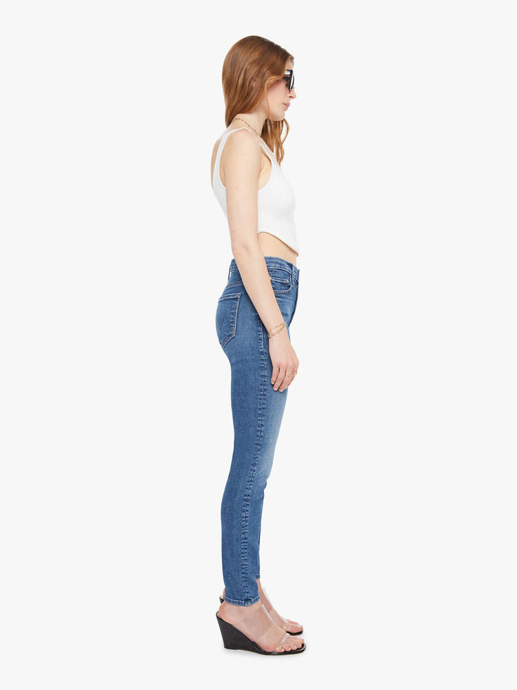 Side view of a woman in a med blue skinny with a high rise with a zip fly, 29-inch inseam and a clean hem. 
