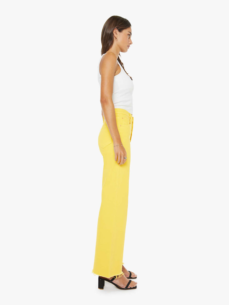 Side view of a woman in yellow high-waisted wide-leg jeans with a button fly, 31-inch inseam and a frayed hem.