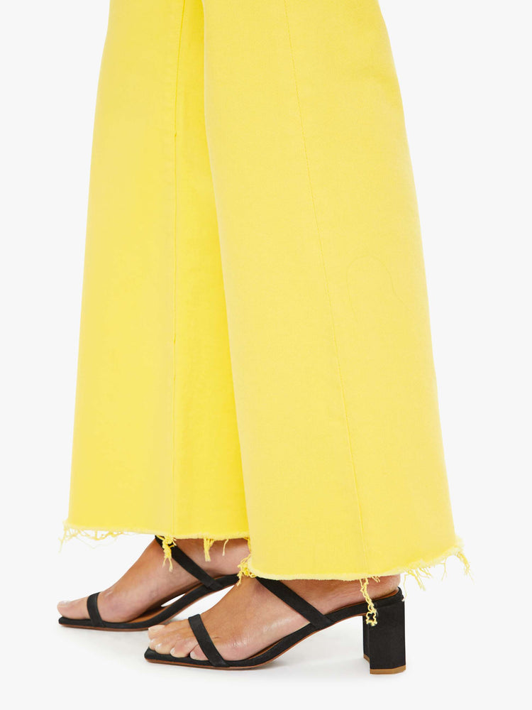Hem close up view of a woman in yellow high-waisted wide-leg jeans with a button fly, 31-inch inseam and a frayed hem.