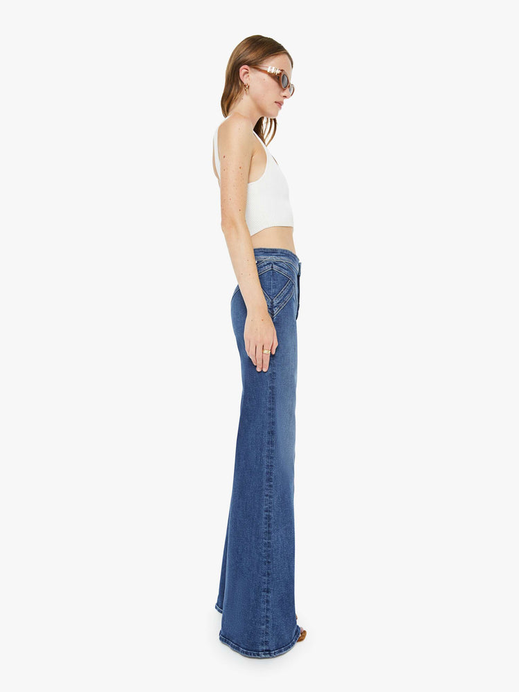 Side view of a woman in a mid blue high-rise wide-leg pants with a zip fly, seamed details on the waist, slit pockets and a long 34-inch inseam with a clean hem. 