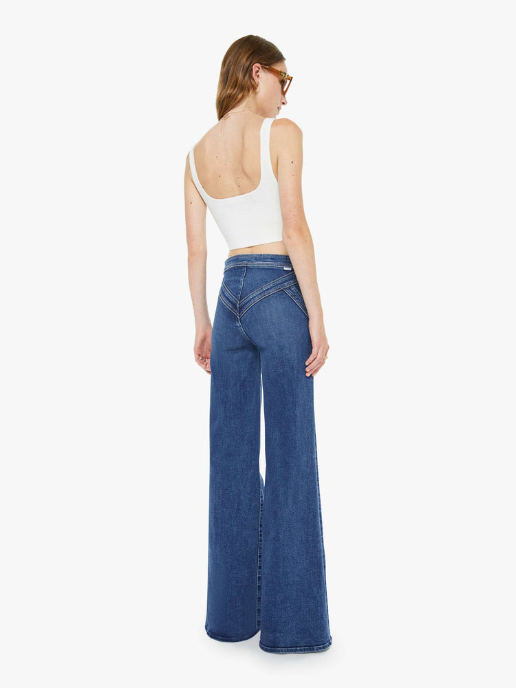 Back view of a woman in a mid blue high-rise wide-leg pants with a zip fly, seamed details on the waist, slit pockets and a long 34-inch inseam with a clean hem. 