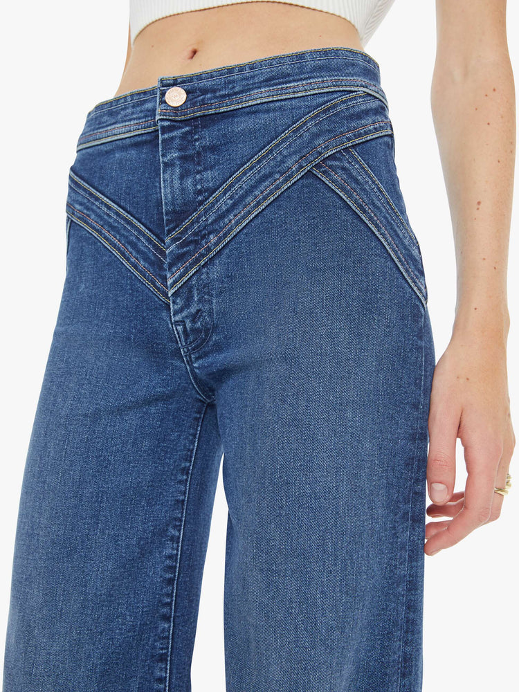 Close up view of a woman in a mid blue high-rise wide-leg pants with a zip fly, seamed details on the waist, slit pockets and a long 34-inch inseam with a clean hem. 