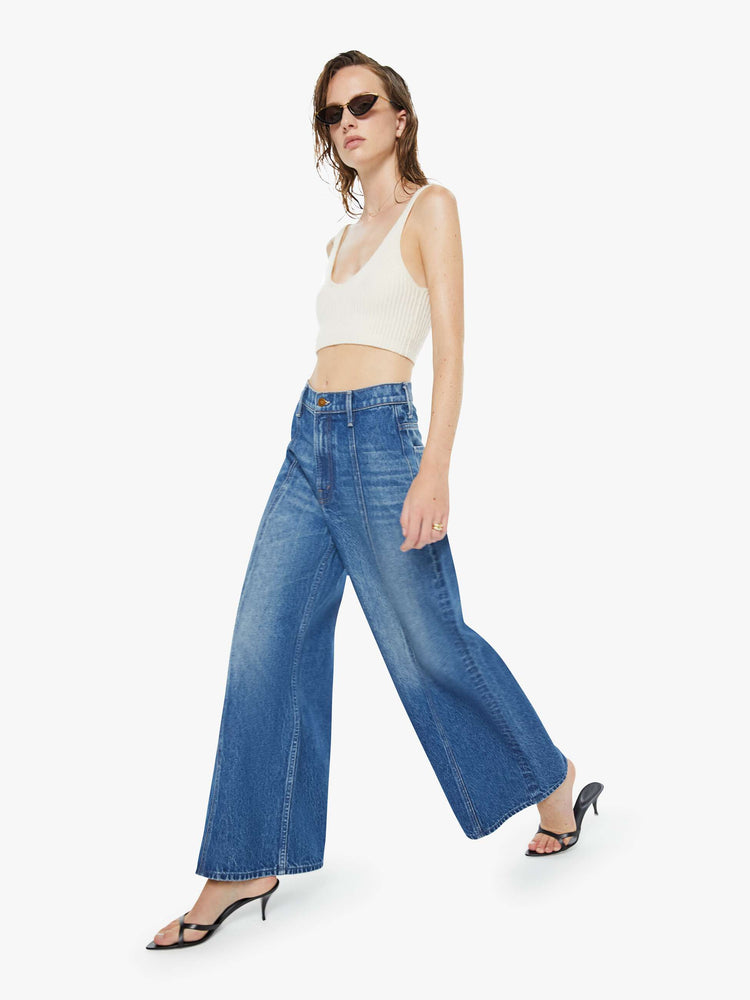 Walking view of a woman in a mid blue  high-waisted pants have a zip fly, loose, wide leg with seamed details down the front and a 28.5-inch inseam with a clean hem. 