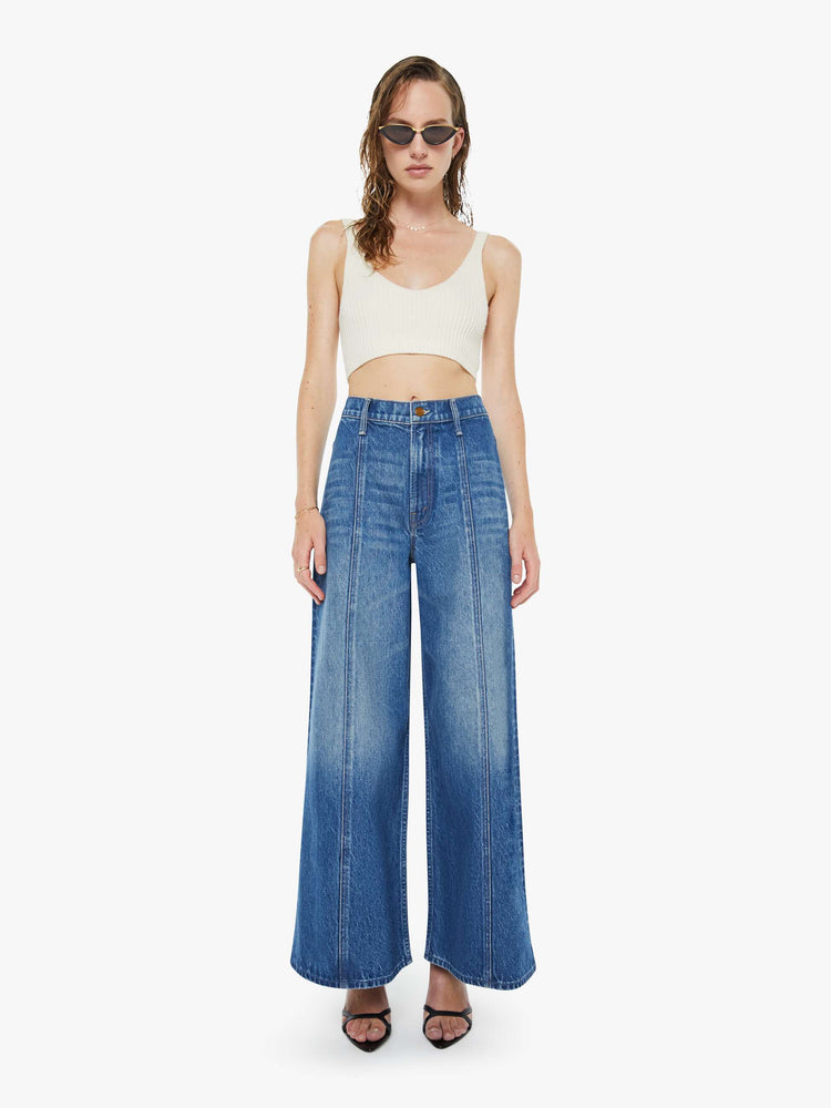 Front view of a woman in a mid blue  high-waisted pants have a zip fly, loose, wide leg with seamed details down the front and a 28.5-inch inseam with a clean hem. 