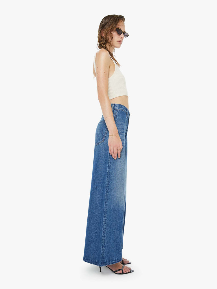 Side view of a woman in a mid blue  high-waisted pants have a zip fly, loose, wide leg with seamed details down the front and a 28.5-inch inseam with a clean hem. 