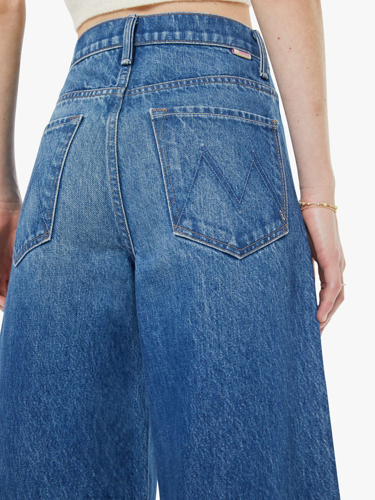 Close up view of a woman in a mid blue  high-waisted pants have a zip fly, loose, wide leg with seamed details down the front and a 28.5-inch inseam with a clean hem. 
