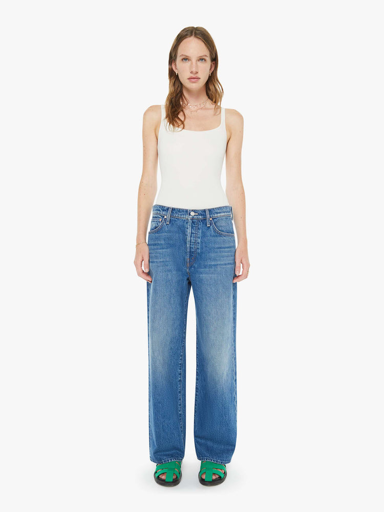 Front view of a woman in a med blue jeans designed to sit on the hips with a slouchy fit, a loose straight leg, button fly and a 28.5-inch inseam with a clean hem.