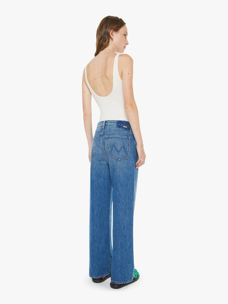 Back view of a woman in a med blue jeans designed to sit on the hips with a slouchy fit, a loose straight leg, button fly and a 28.5-inch inseam with a clean hem.