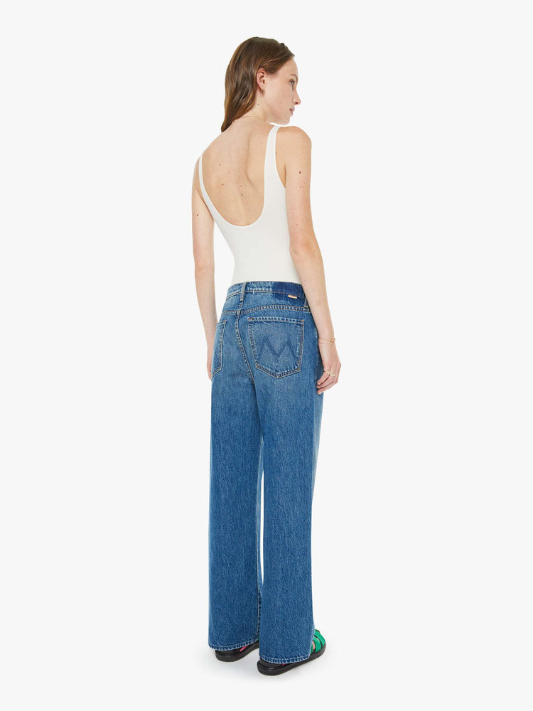 Back view of a woman in a med blue jeans designed to sit on the hips with a slouchy fit, a loose straight leg, button fly and a 28.5-inch inseam with a clean hem.