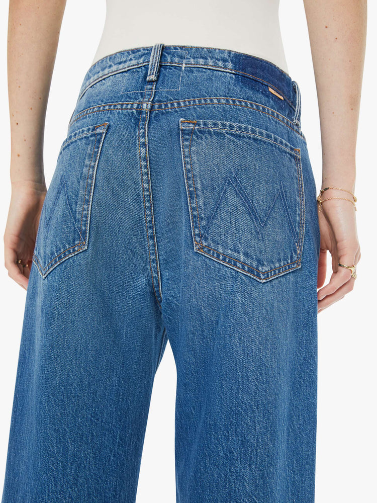 Back view of a woman in a med blue jeans designed to sit on the hips with a slouchy fit, a loose straight leg, button fly and a 28.5-inch inseam with a clean hem.