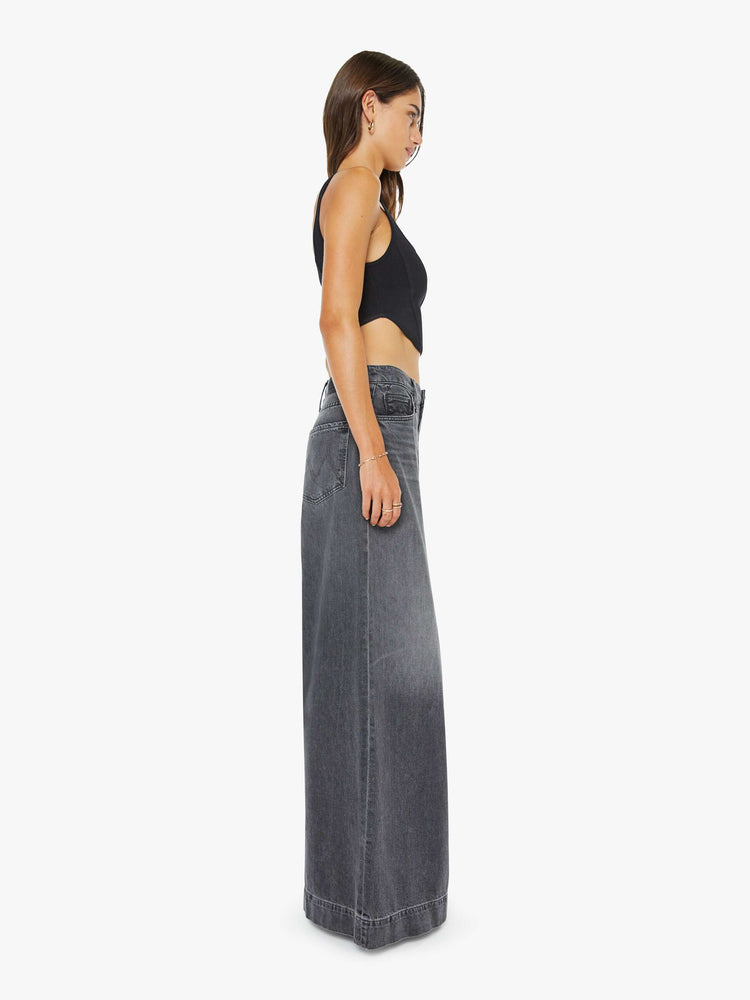 Side view of a woman in a faded black mid-rise wide-leg jeans with a zip fly, long 34-inch inseam and a clean, wide hem.