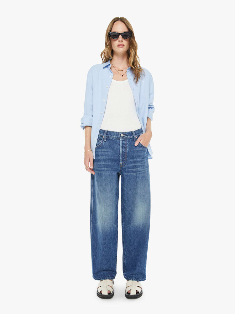 Front view of a woman in a mid blue jeans designed to sit lower on the hips with an ankle-length inseam, button fly, clean hem and slightly tapered leg. 