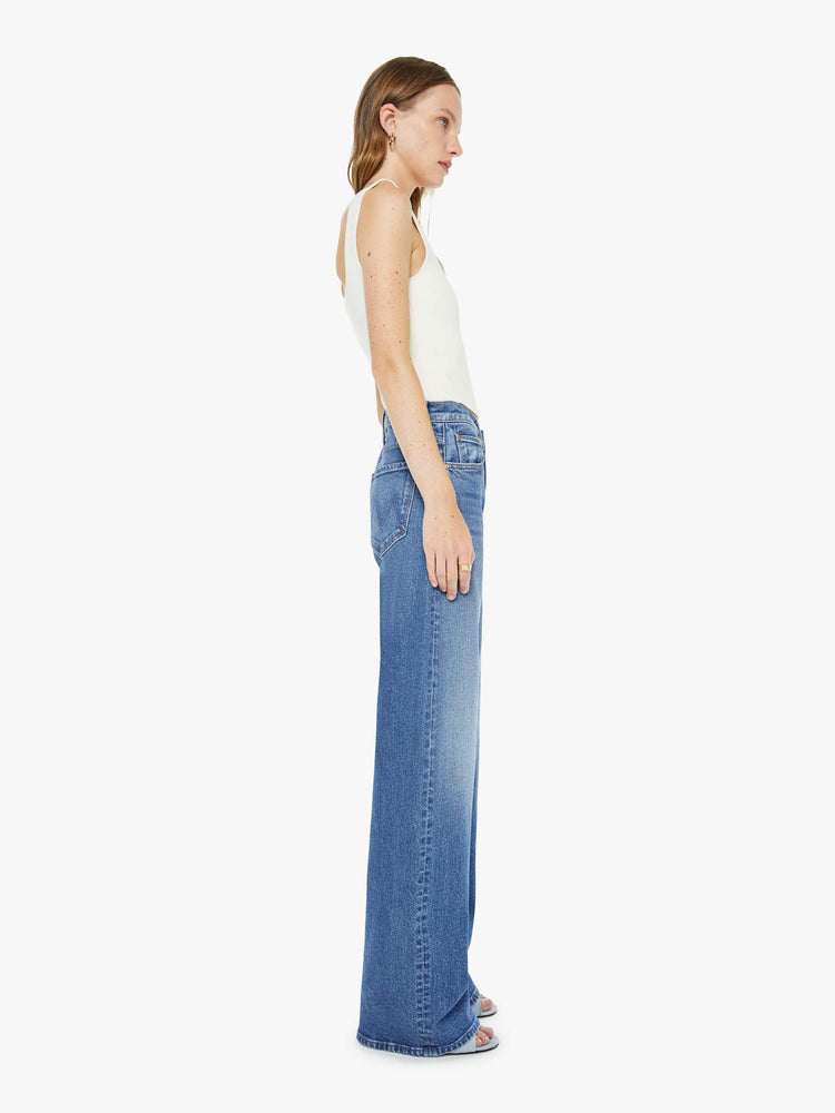 Side view of a woman in med blue wide-leg pants with a zip fly, mid rise and a long 34-inch inseam with a clean hem.