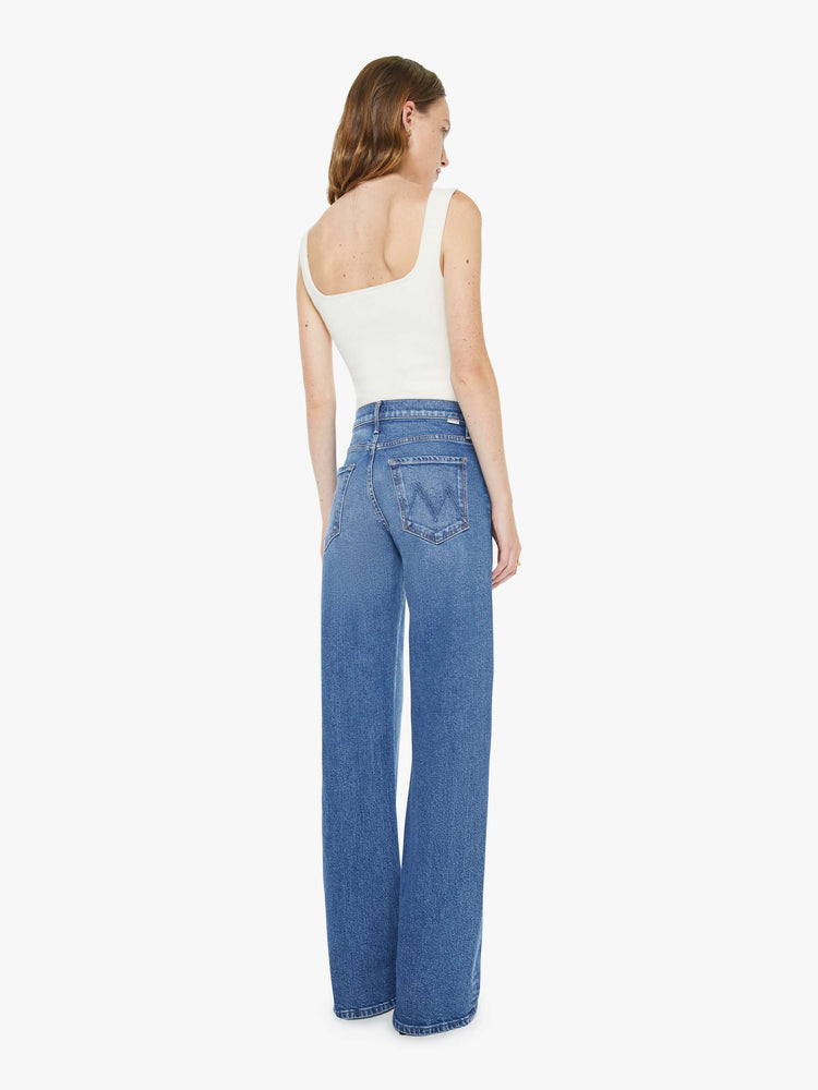 Back view of a woman in med blue wide-leg pants with a zip fly, mid rise and a long 34-inch inseam with a clean hem.