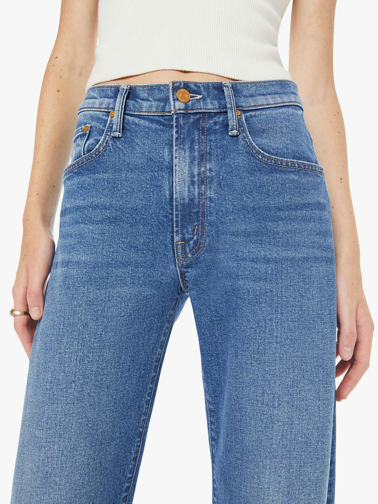 Close up view of a woman in med blue wide-leg pants with a zip fly, mid rise and a long 34-inch inseam with a clean hem.