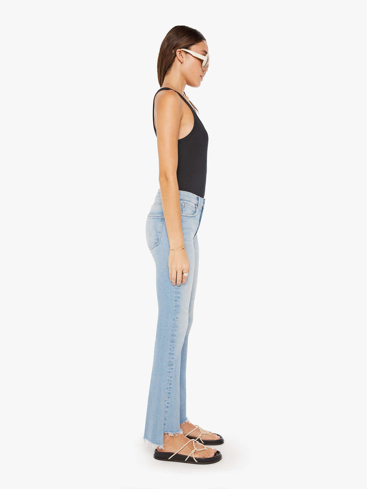 Side view of a womens light blue denim featuring a mid rise, flare leg, and a crop step fray hem.