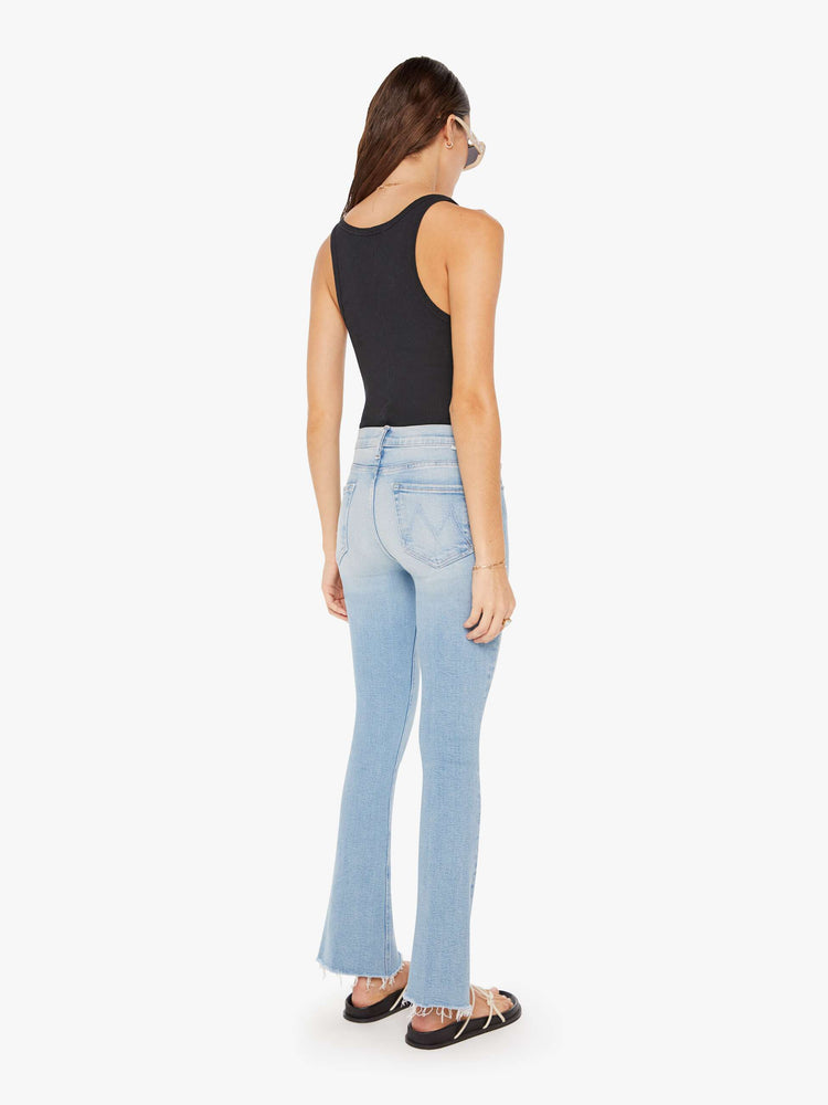 Back view of a womens light blue denim featuring a mid rise, flare leg, and a crop step fray hem.