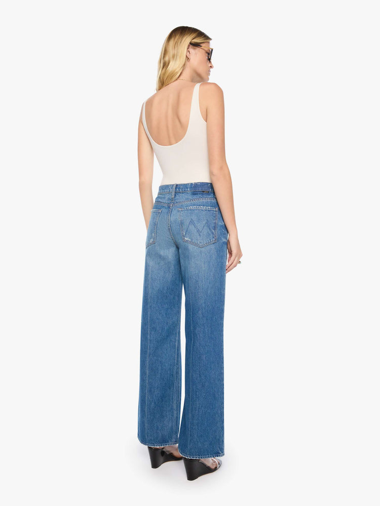 Back view of a woman in a med blue with tears in the knees high-waisted wide leg jeans with a button fly, 32-inch inseam and loose, low-slung fit. 