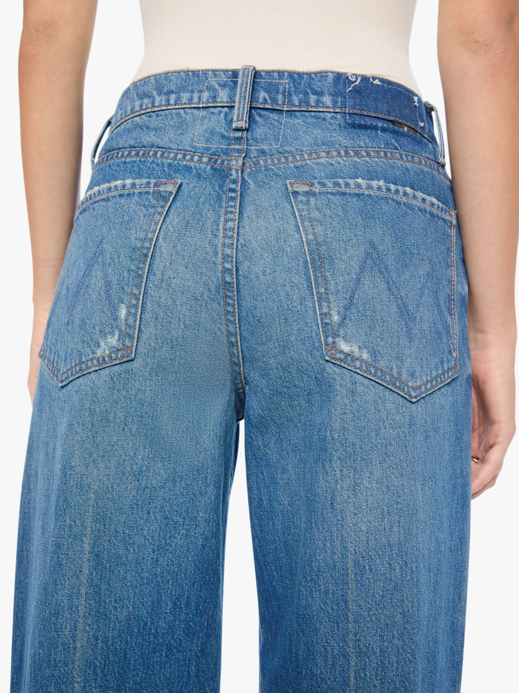 Back close up view of a woman in a med blue with tears in the knees high-waisted wide leg jeans with a button fly, 32-inch inseam and loose, low-slung fit. 