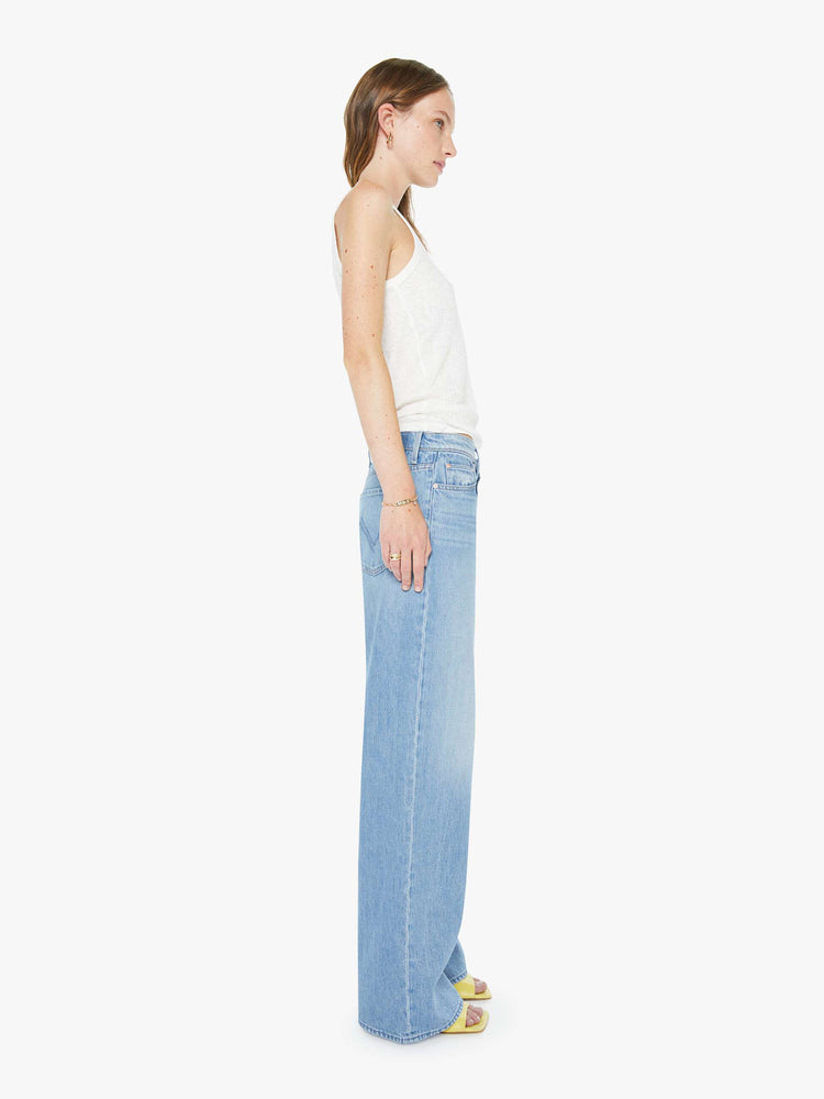 Side view of a woman in a light blue high-waisted wide leg jeans with a zip fly, a long 32-inch inseam and loose, low-slung fit.