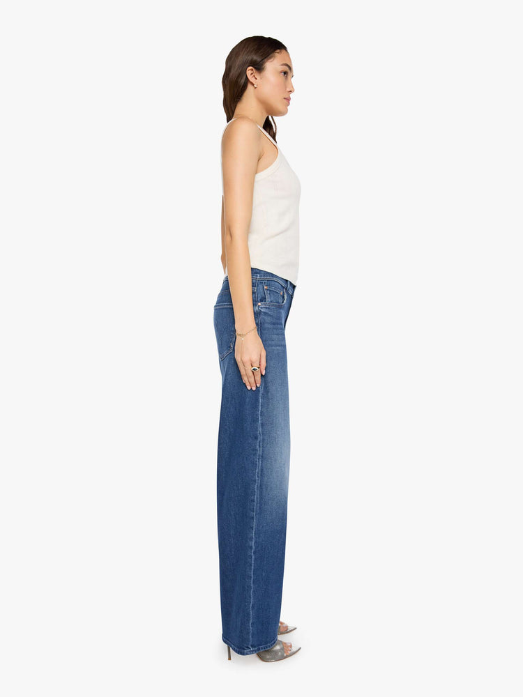 Side view of a woman in a mid blue high-waisted wide leg jeans with a zip fly, 33-inch inseam and loose, low-slung fit.
