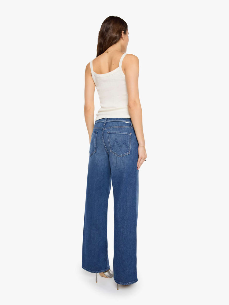 Back view of a woman in a mid blue high-waisted wide leg jeans with a zip fly, 33-inch inseam and loose, low-slung fit.