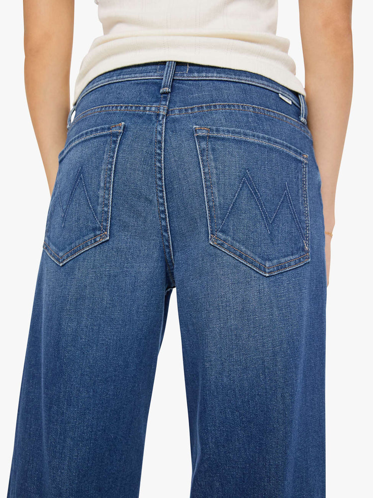 Close up view of a woman in a mid blue high-waisted wide leg jeans with a zip fly, 33-inch inseam and loose, low-slung fit.