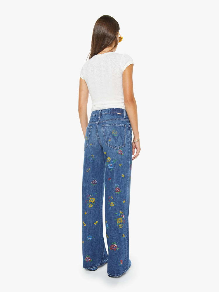 Back view of a woman in a mid blue with flowers high-waisted wide leg jeans with a zip fly, a long 32-inch inseam and loose, low-slung fit.
