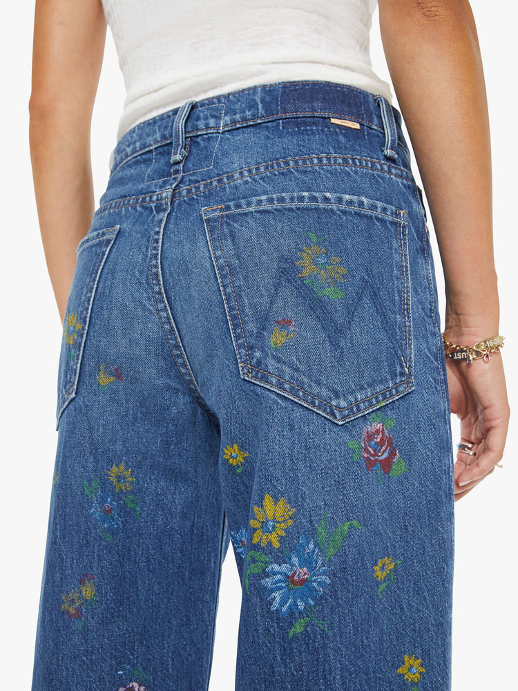 Close up view of a woman in a mid blue with flowers high-waisted wide leg jeans with a zip fly, a long 32-inch inseam and loose, low-slung fit.