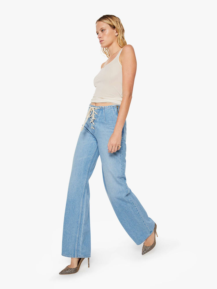 Walking view of a woman in a light blue low-slung jeans are designed with a laced closure at the front, a side zip and a wide leg with a 32-inch inseam and a clean hem.