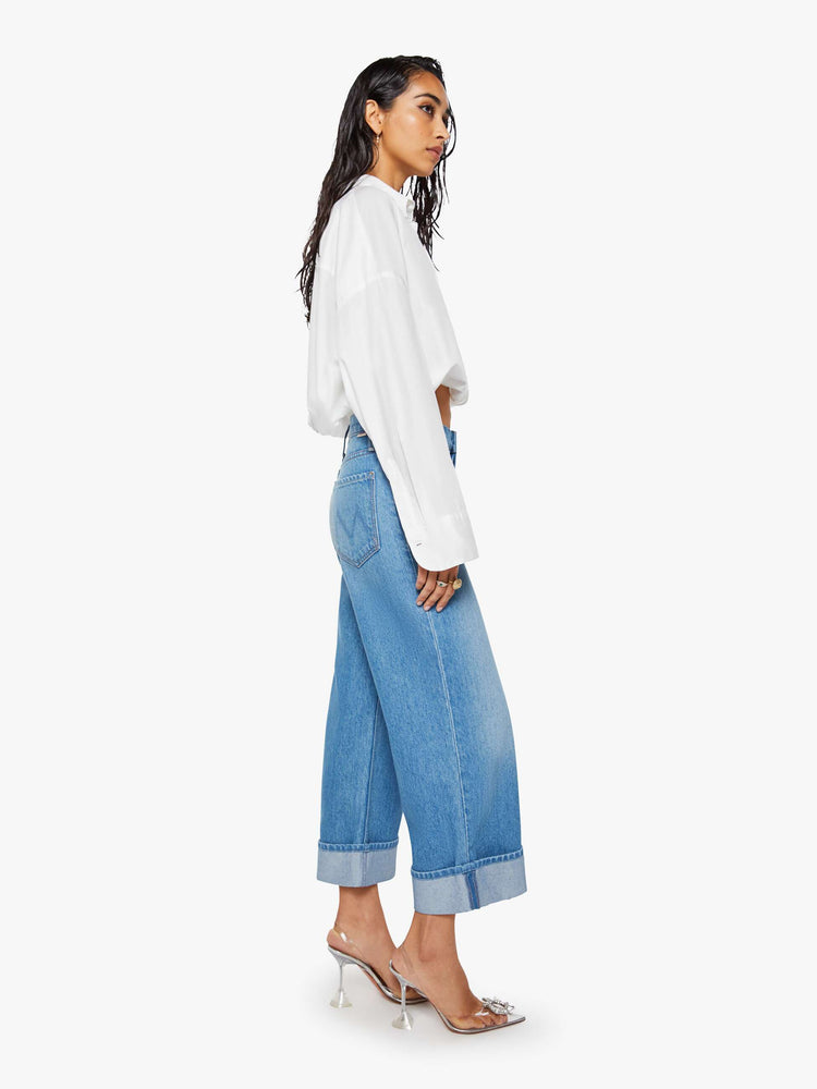 Side view of a woman in mid blue wide-leg jeans are designed with a button fly and a 26-inch inseam with a cuffed hem.