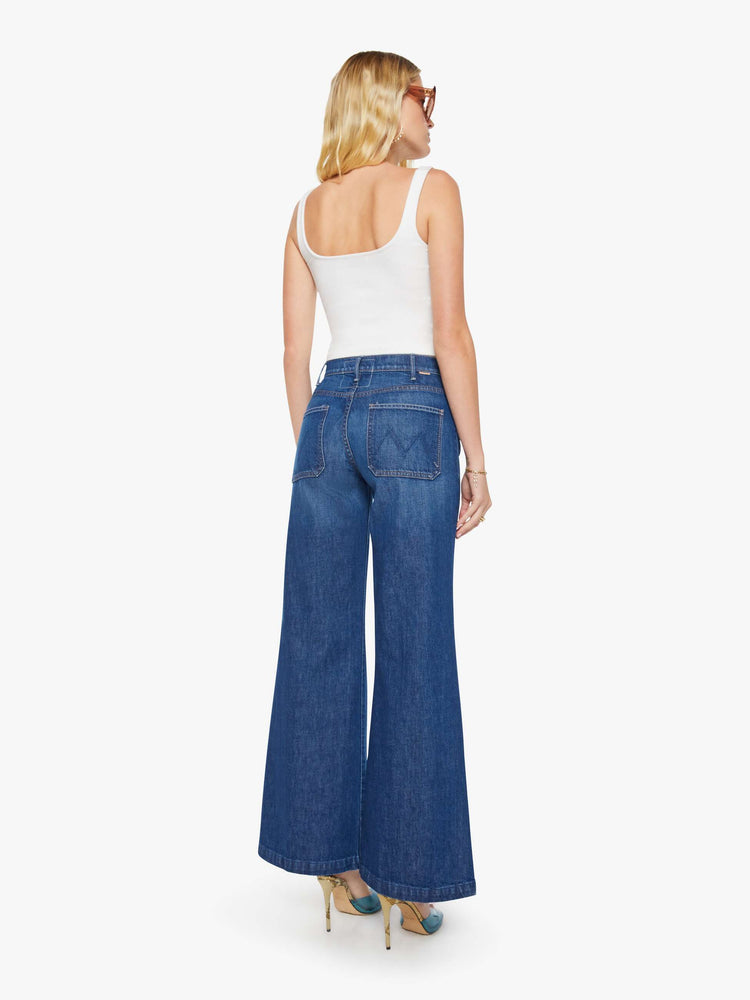 Back view of a woman in a dark blue wide leg jeans with a high rise, exposed zip fly, tabbed waistband, patch pockets and a long 34-inch inseam with a clean hem.