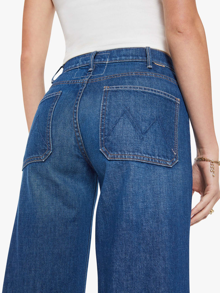 Close up view of a woman in a dark blue wide leg jeans with a high rise, exposed zip fly, tabbed waistband, patch pockets and a long 34-inch inseam with a clean hem.