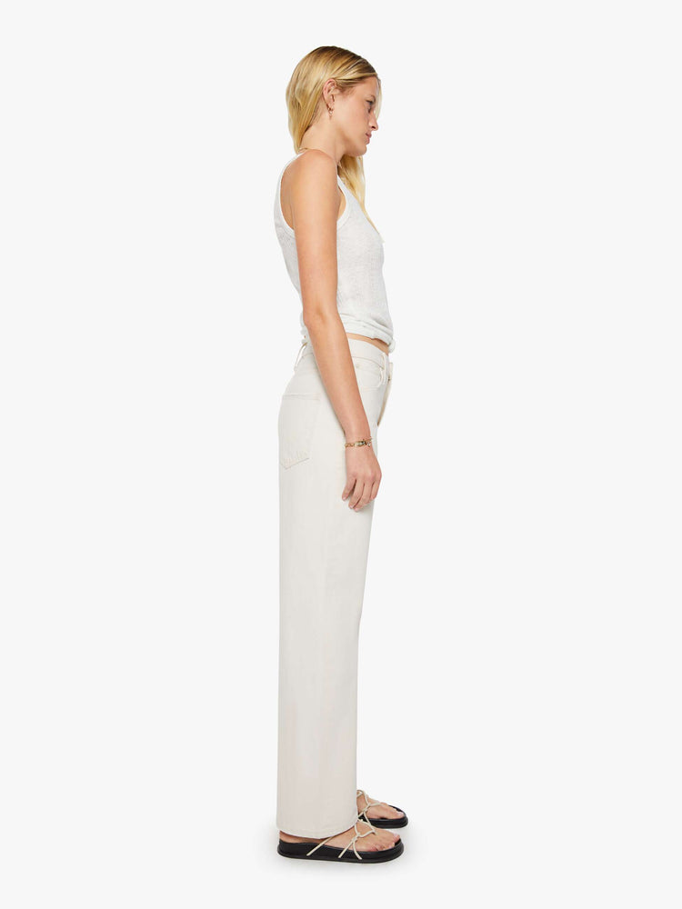 Side view of a woman in creamy white pants designed to sit lower on the hips with a zip fly, loose straight leg and a clean 31-inch inseam.