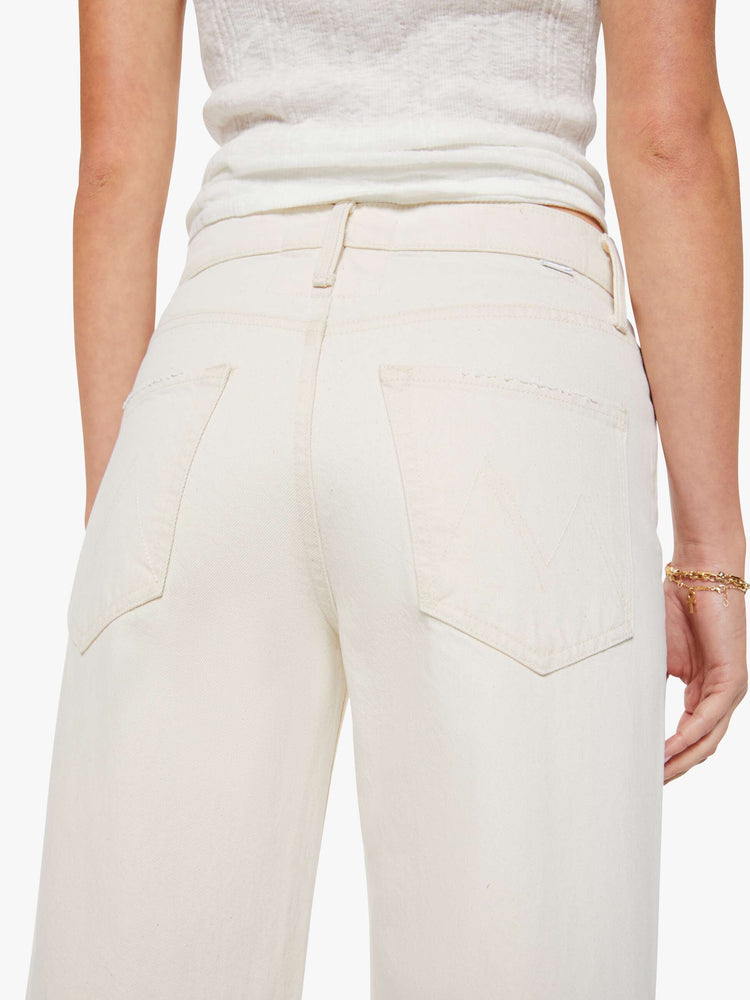Back view of a woman in creamy white pants designed to sit lower on the hips with a zip fly, loose straight leg and a clean 31-inch inseam.