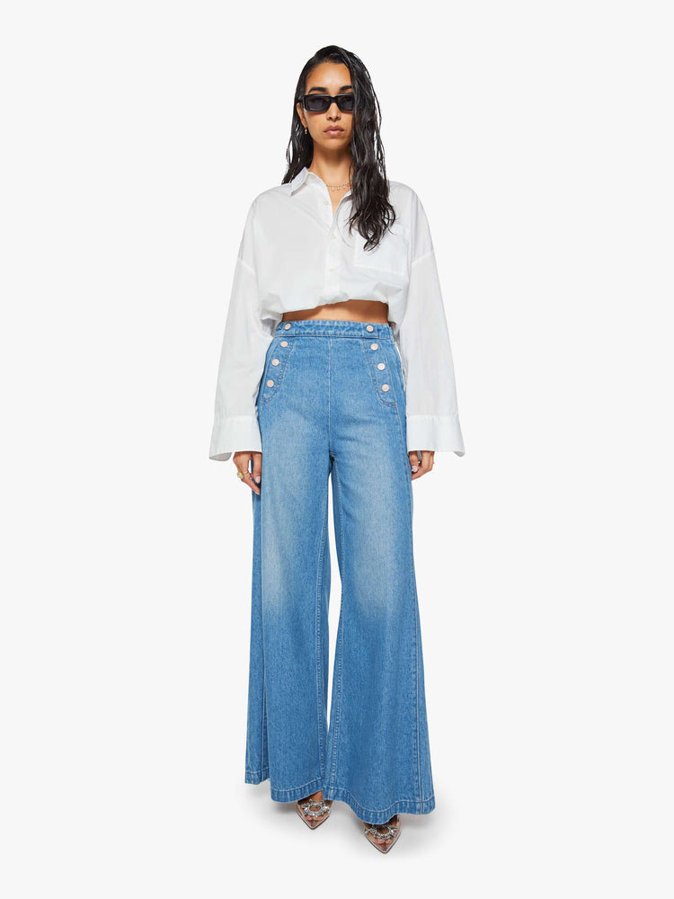 Front view of a woman in a med blue super high-waisted jeans have a loose, wide leg, sailor-inspired buttons on the front, a left side zipper and a long 32-inch inseam with a clean hem.