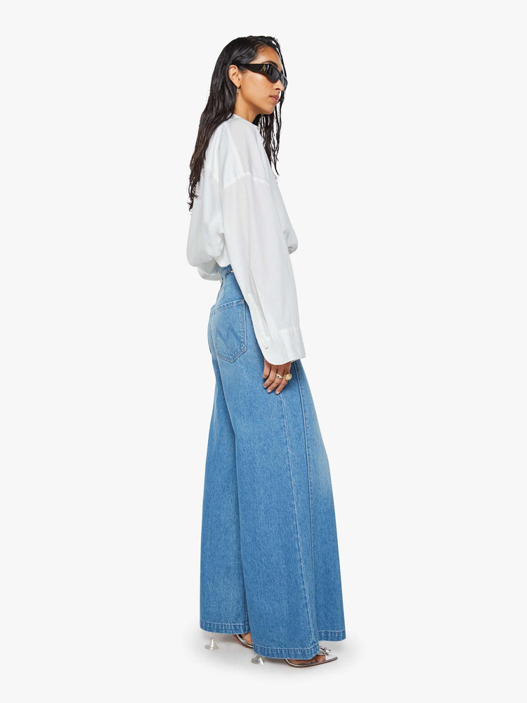 Side view of a woman in a med blue super high-waisted jeans have a loose, wide leg, sailor-inspired buttons on the front, a left side zipper and a long 32-inch inseam with a clean hem.