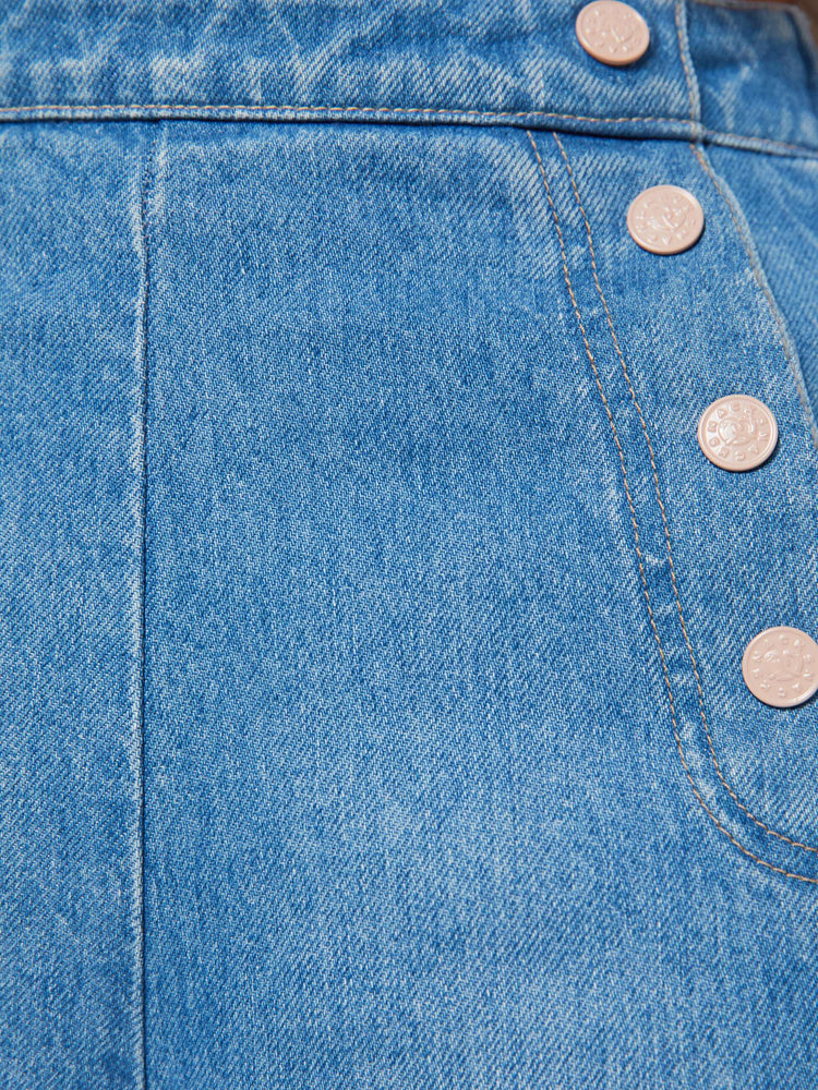 Close up view of a woman in a med blue super high-waisted jeans have a loose, wide leg, sailor-inspired buttons on the front, a left side zipper and a long 32-inch inseam with a clean hem.