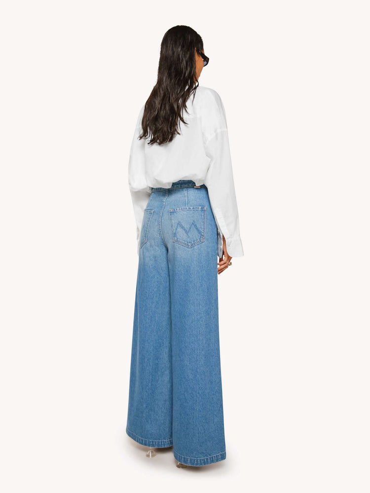 Back view of a woman in a med blue super high-waisted jeans have a loose, wide leg, sailor-inspired buttons on the front, a left side zipper and a long 32-inch inseam with a clean hem.