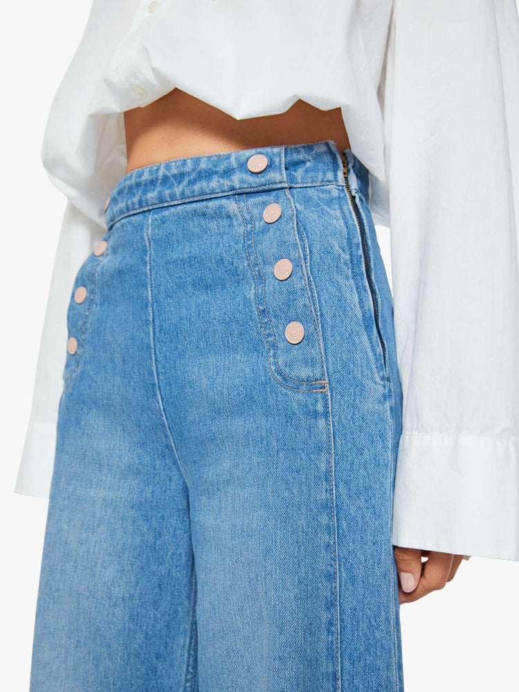 Close up view of a woman in a med blue super high-waisted jeans have a loose, wide leg, sailor-inspired buttons on the front, a left side zipper and a long 32-inch inseam with a clean hem.