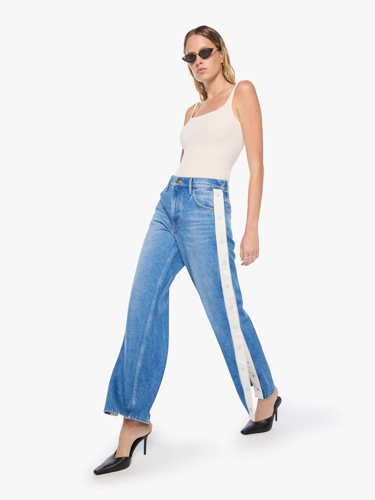 Walking view of mid blue high-waisted jeans have a loose, low-slung fit, zip fly, a white stripe down the outer seam with adjustable snaps, a long 31-inch inseam and a clean hem.