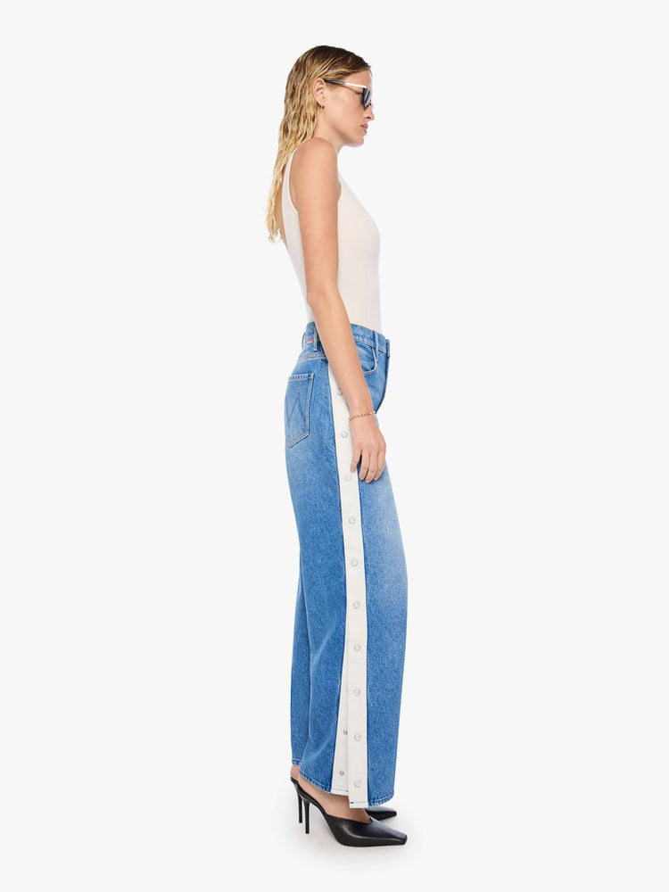 Side view of mid blue high-waisted jeans have a loose, low-slung fit, zip fly, a white stripe down the outer seam with adjustable snaps, a long 31-inch inseam and a clean hem.
