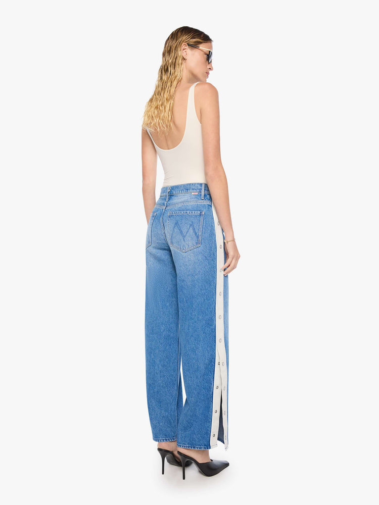 Back view of mid blue high-waisted jeans have a loose, low-slung fit, zip fly, a white stripe down the outer seam with adjustable snaps, a long 31-inch inseam and a clean hem.