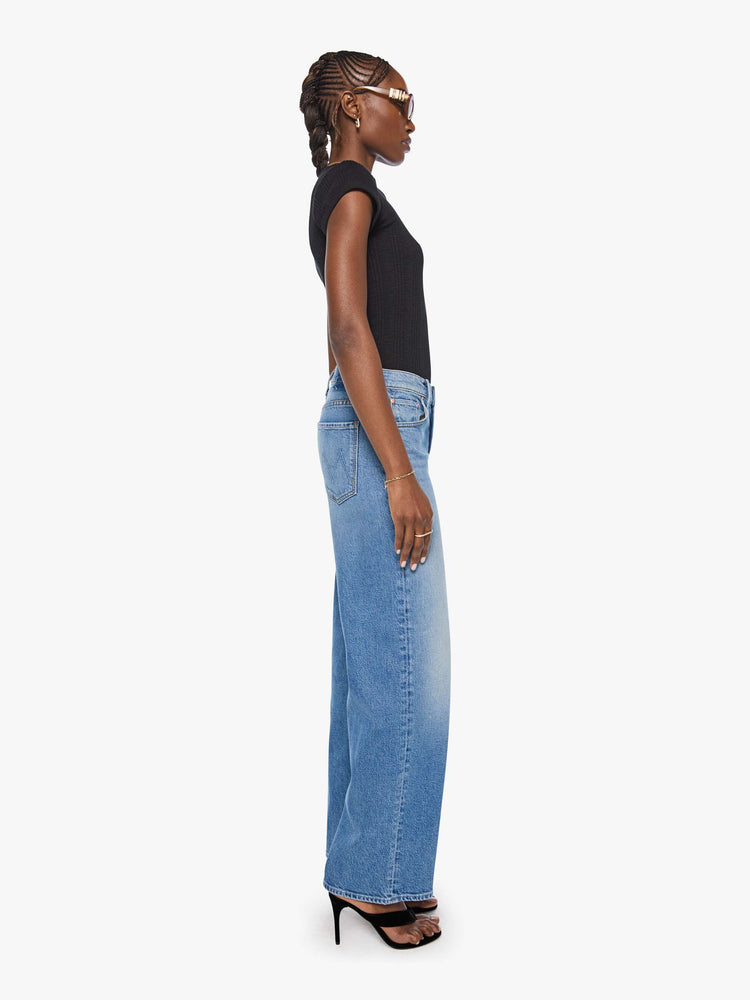 Side view of a woman in a med blue high-waisted wide leg jeans with a zip fly, a long 31-inch inseam and loose, low-slung fit. 