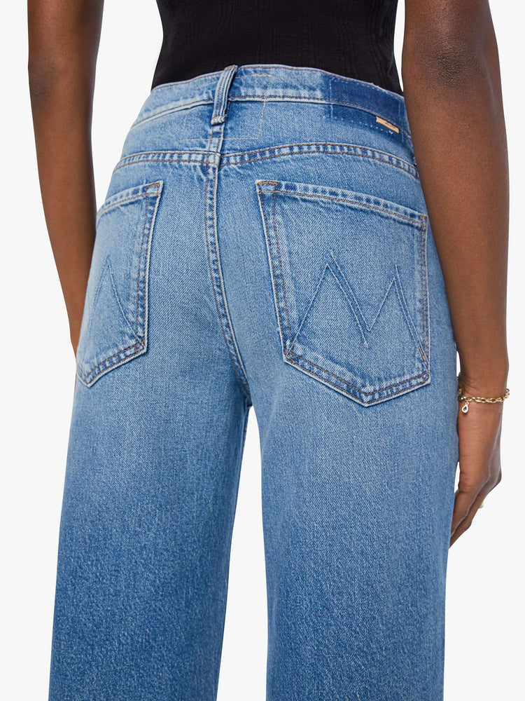 Close up view of a woman in a med blue high-waisted wide leg jeans with a zip fly, a long 31-inch inseam and loose, low-slung fit. 