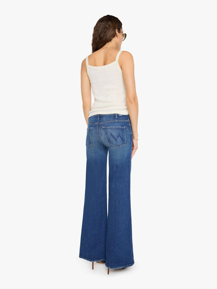 Back view of a woman in a mid blue wide leg jeans with a high rise, zip fly, double-stitched side seam, 32-inch inseam and a clean hem.