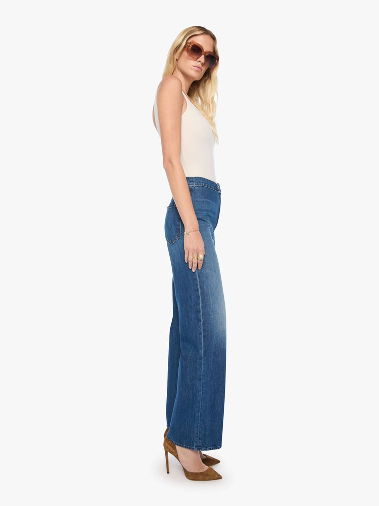 Side view of a woman in med blue high-rise wide-leg jeans with a zip fly, button-tab waistband, a long 32-inch inseam and a loose, low-slung fit. 