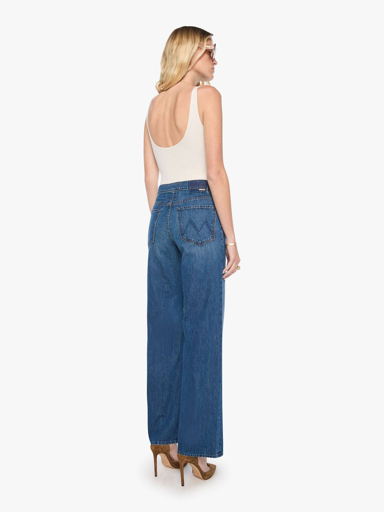 Back view of a woman in med blue high-rise wide-leg jeans with a zip fly, button-tab waistband, a long 32-inch inseam and a loose, low-slung fit. 